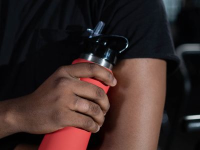 Hands holding a sports bottle in a dark gym.